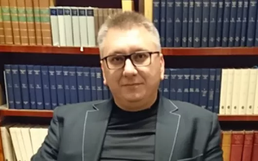 zdjęcie Roberta Cichowicza siedzącego w gabinecie na tle biblioteczki z książkami